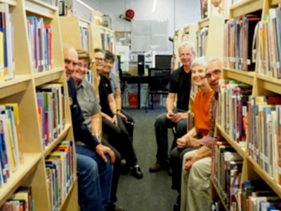 Volunteers sitting between the shelves and books of the Lax Kw'alaam library.